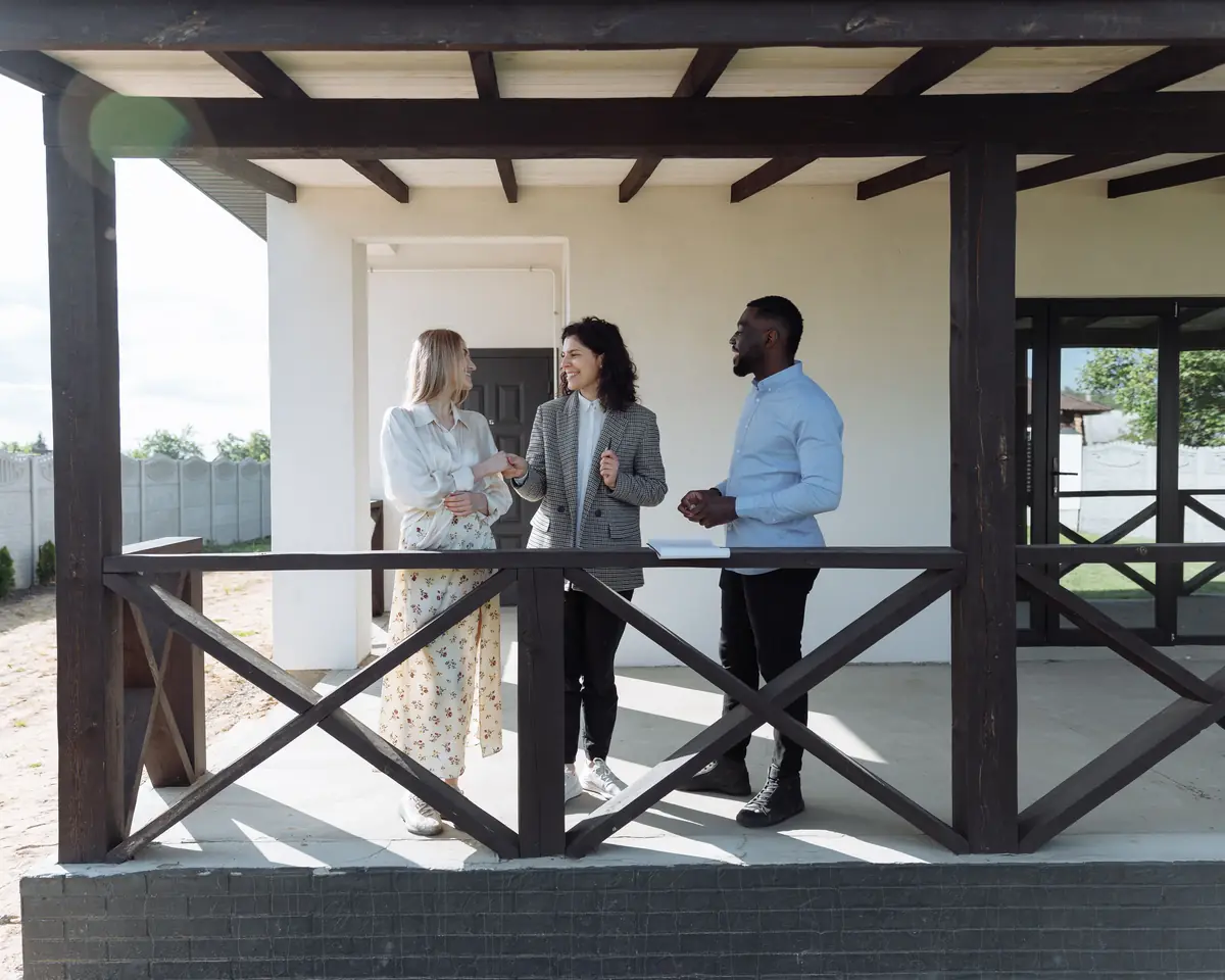 An agent talking with a couple on the porch of a new home