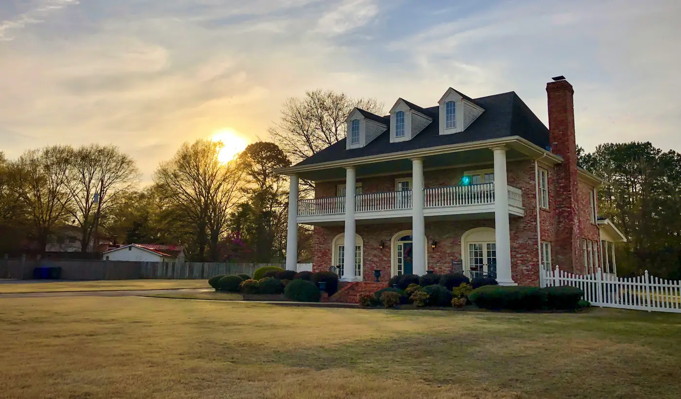 A brick colonial home with a front porch at sunset